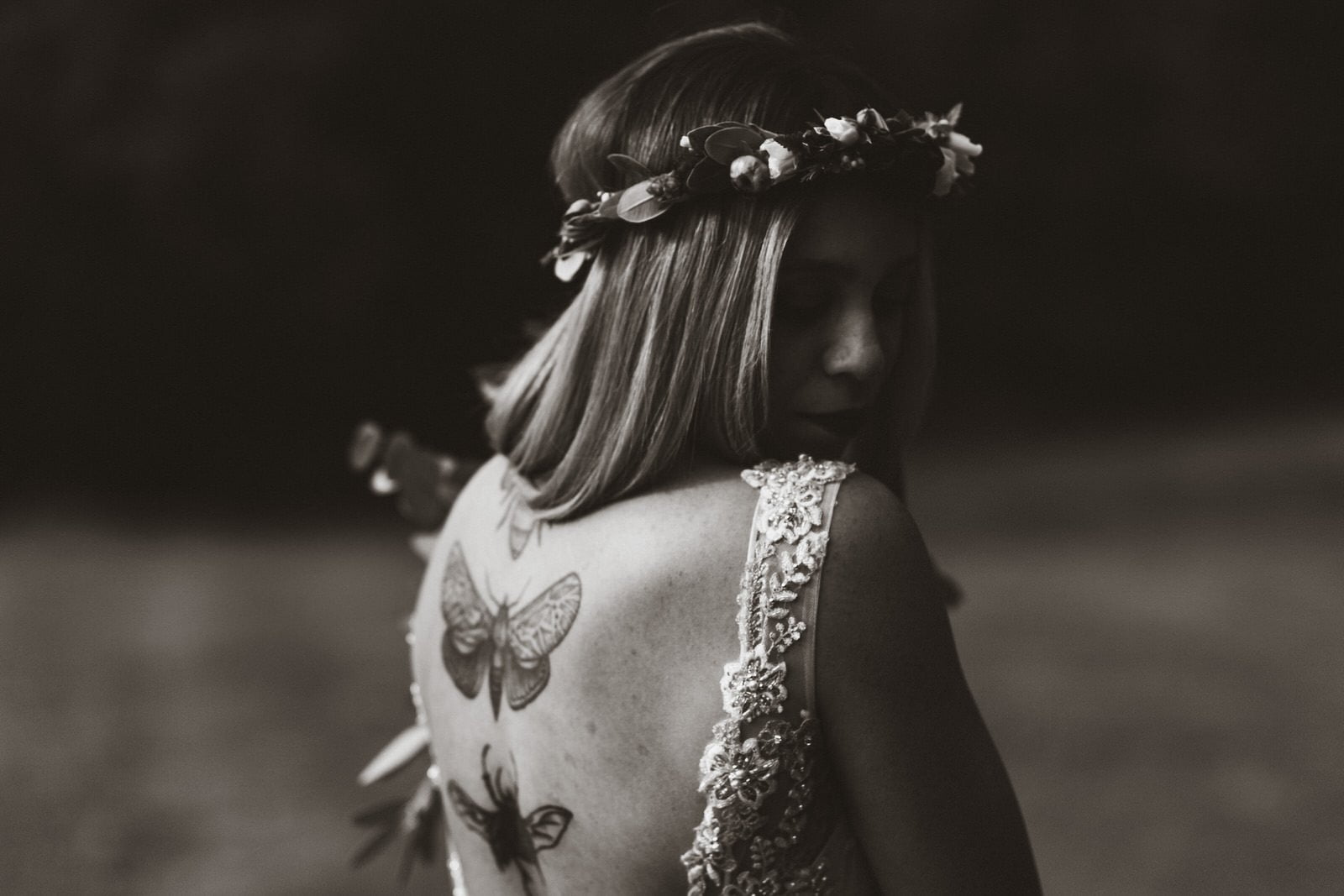 Black and white photography of Holly with her back towards the camera and her head turned to look over her shoulder. Her butterfly tattoos are the main focus