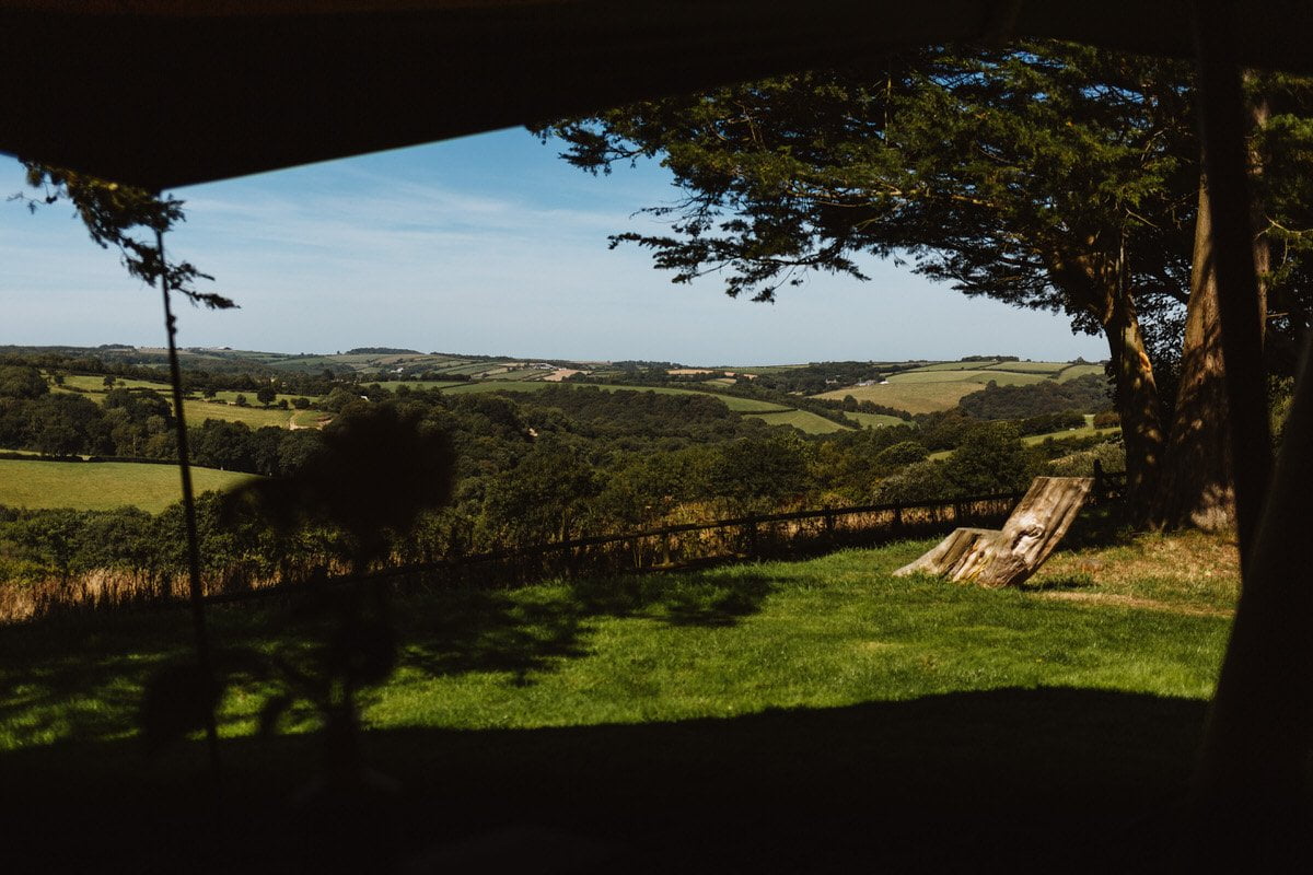 UK wedding photographer takes a snap of a bride in her dressing gown waving and smiling in the doorway of her cottage