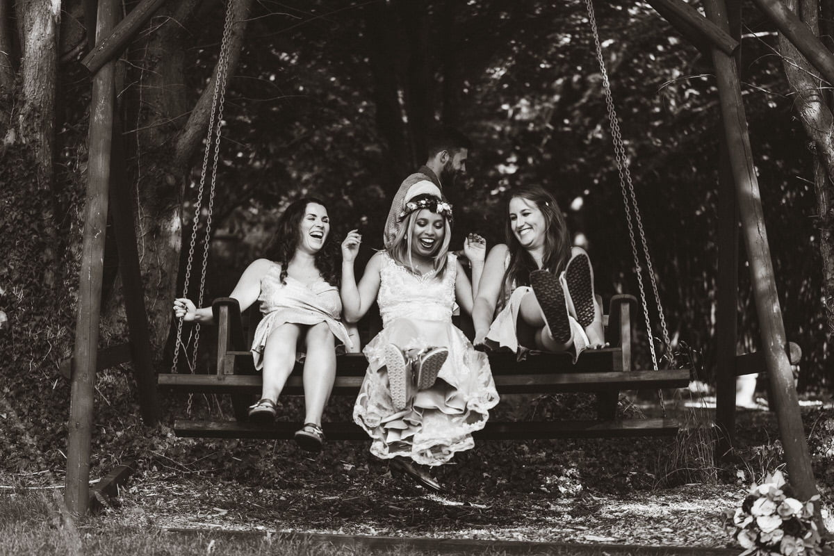 Holly and her two bridesmaids shocked laughing in a garden swing as james sneaks away after pushing them.