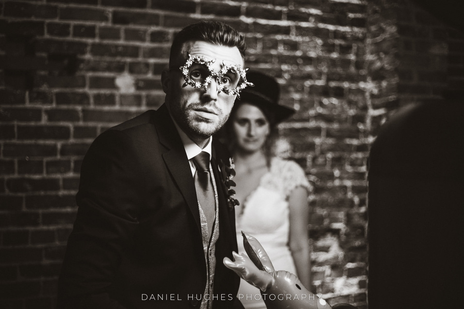 Black and white shot of a male guest in sparkly Christmas glasses at the Hudson Booth, with the bride blurred in the background wearing a top hat.