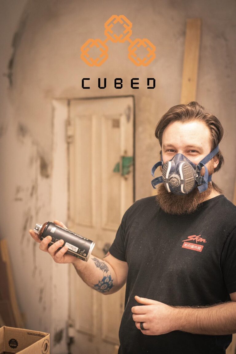 Jonny Flestead from Cubed Cuts and Coffee holding a spray can with a dust mask next to a door.