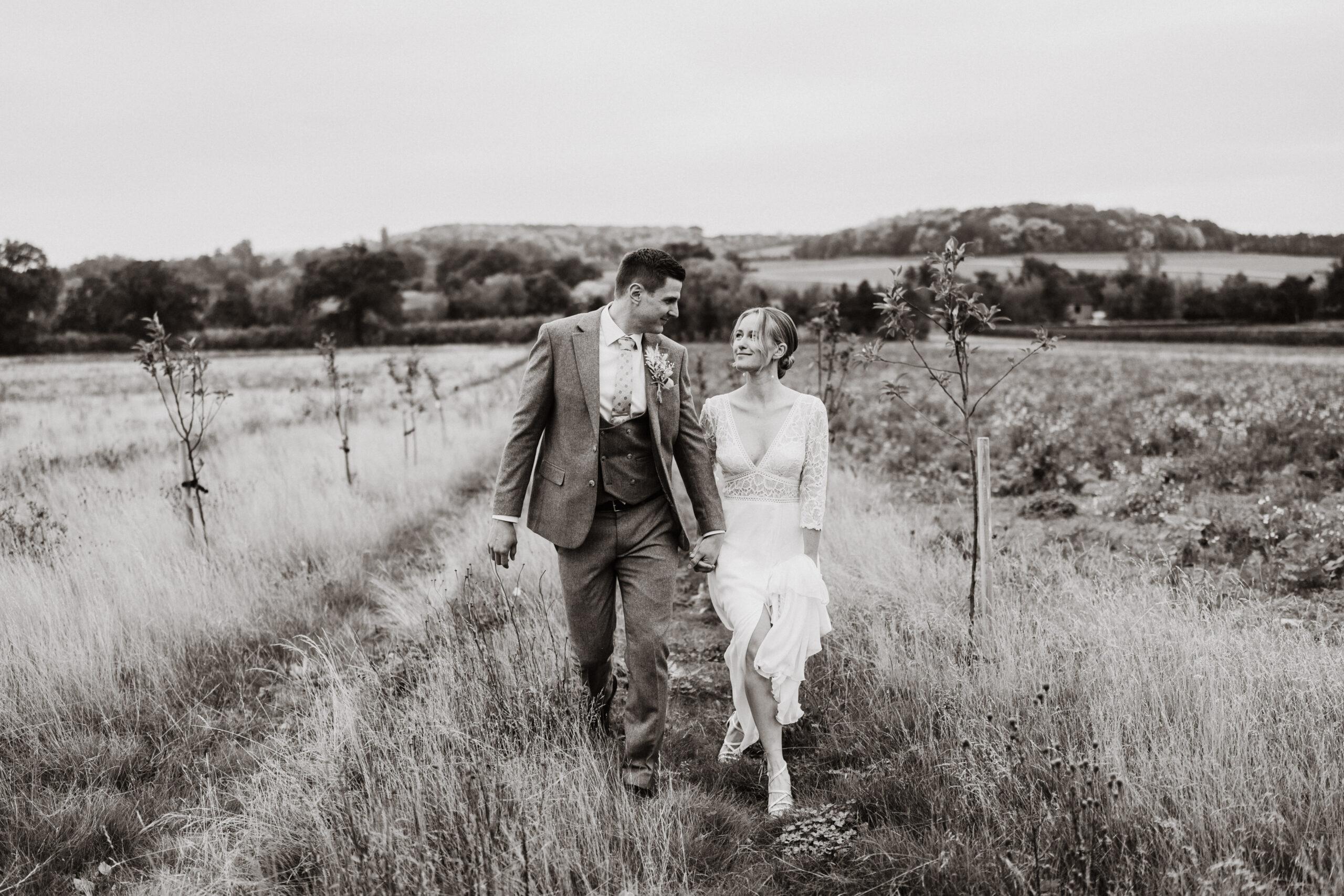 Bride and groom stroll through field at Swallows Nest Barn, authentic wedding portraits without posing